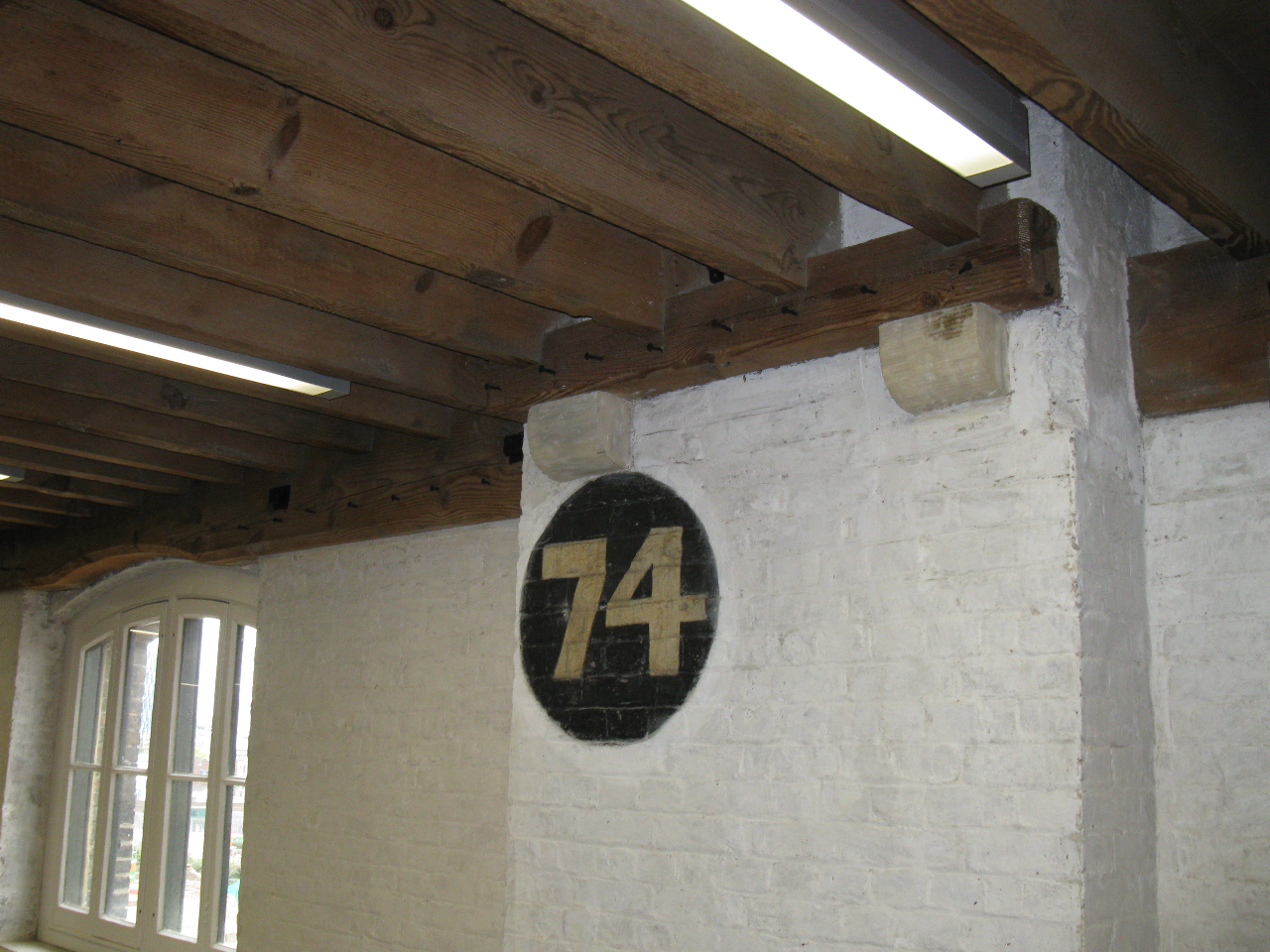 Section of whitewashed brick wall featuring a dark painted circular disk containing the number 74
